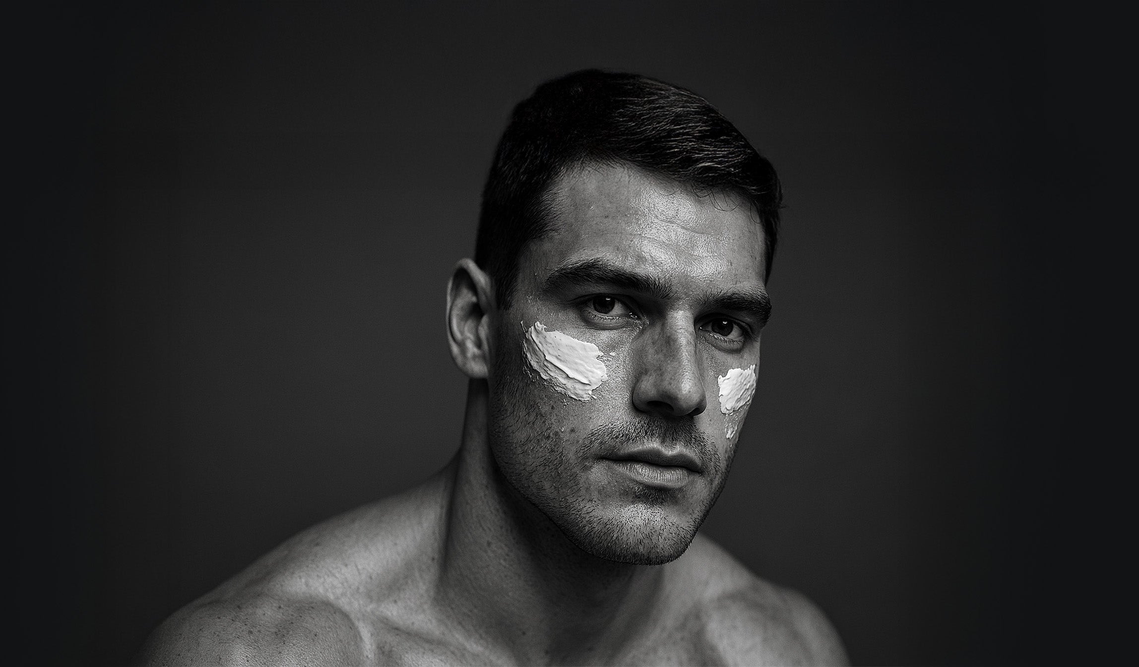 Black and white portrait of a man with face cream on his cheeks - Greens for People high-performance skincare for men.